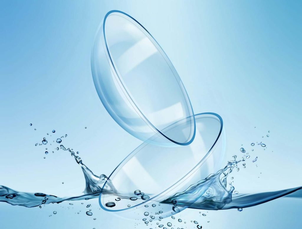 Two soft contact lenses resting above a splash of water