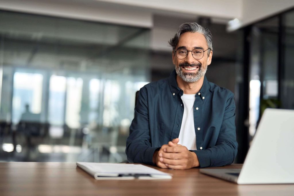 A man wearing his new prescription glasses, smiling at his desk