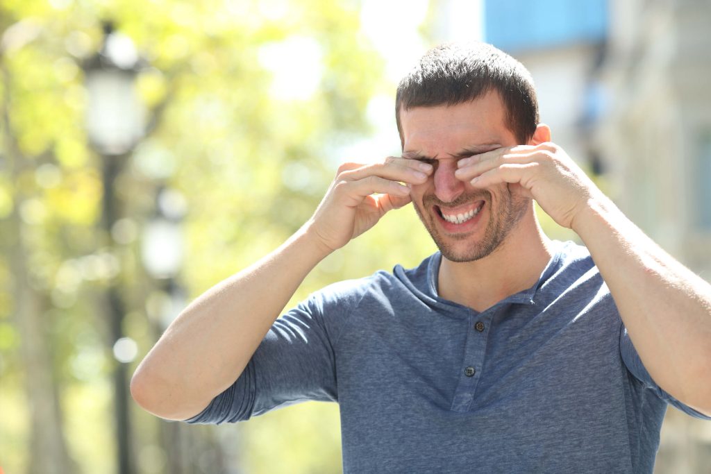Man outdoors rubbing his itchy eye during allergy season